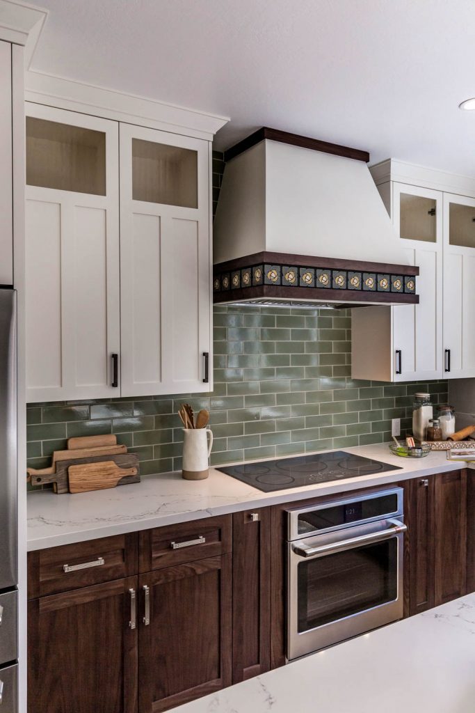 a green backsplash combined with the floral design on the range hood adds visual interest around these remodeled kitchen cabinets